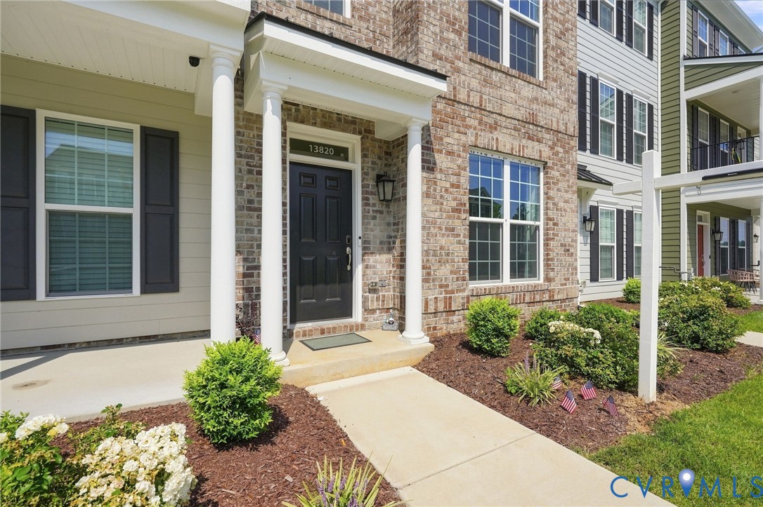 Brick and siding exterior with a paneled front door, white columns, and a concrete walkway Brick and siding exterior with a paneled front door, white columns, and a concrete walkway