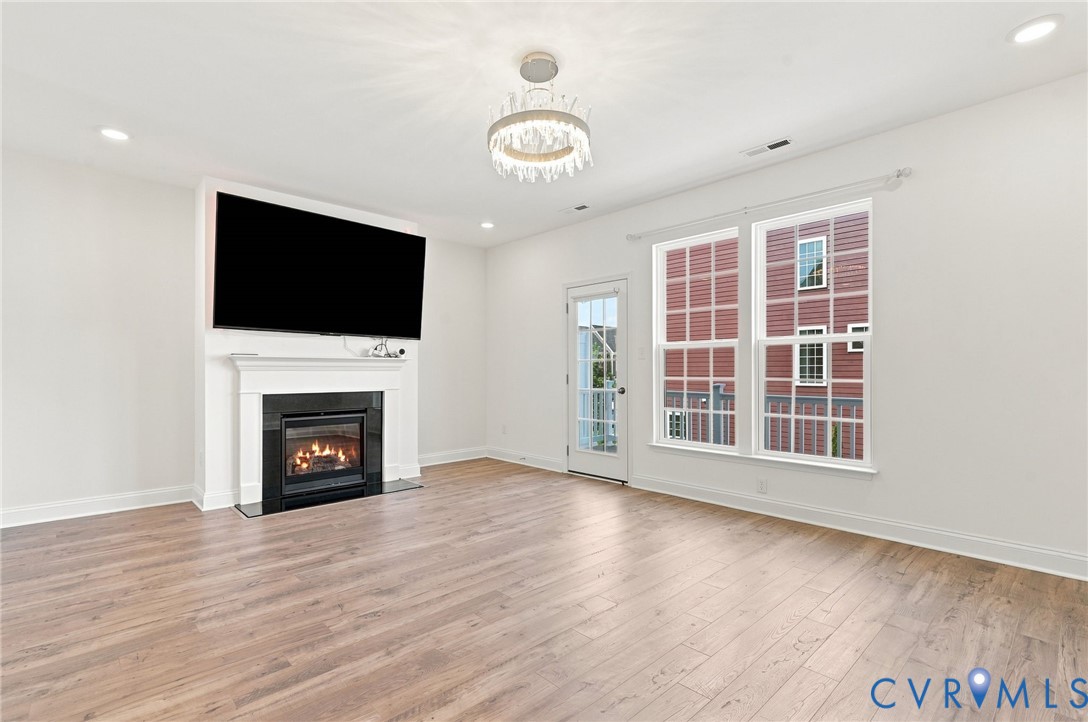 Wood-finish flooring, recessed lighting, and a fireplace with a white mantel and black surround