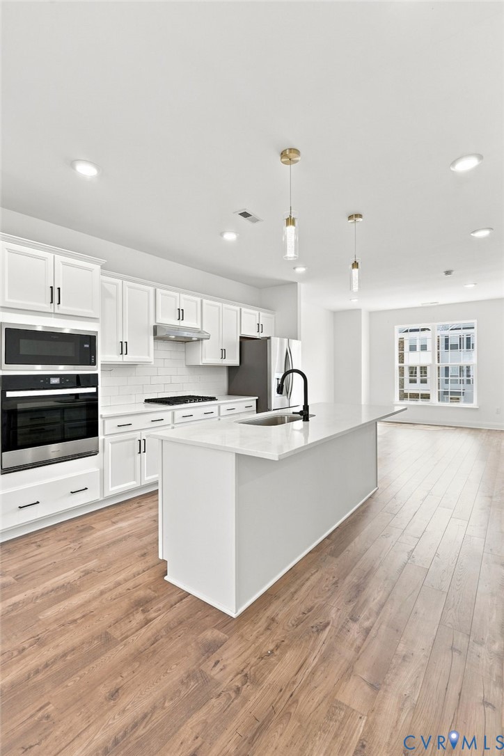 Modern kitchen featuring white shaker cabinetry, stainless steel appliances, a center island with sink, wood-finish flooring, and recessed lighting