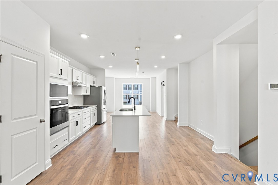 Open-concept kitchen with white shaker cabinetry, stainless steel appliances, and a central island with a sink and pendant lighting