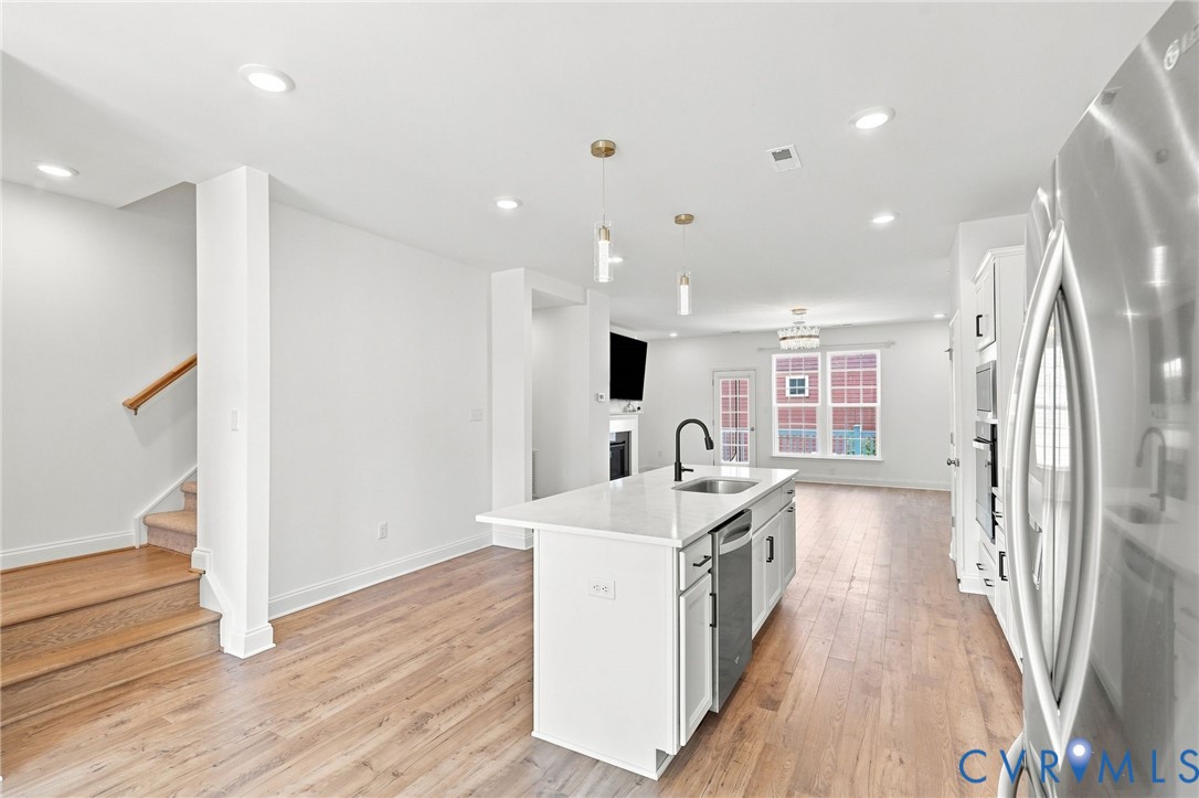 Open-concept layout featuring wood-finish flooring throughout, a central kitchen island with seating, recessed lighting, and stainless steel appliances