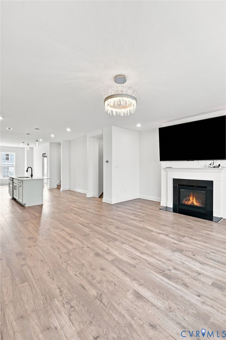 Spacious living area featuring wood-finish flooring, a contemporary fireplace with a white mantel, and a decorative ceiling fixture