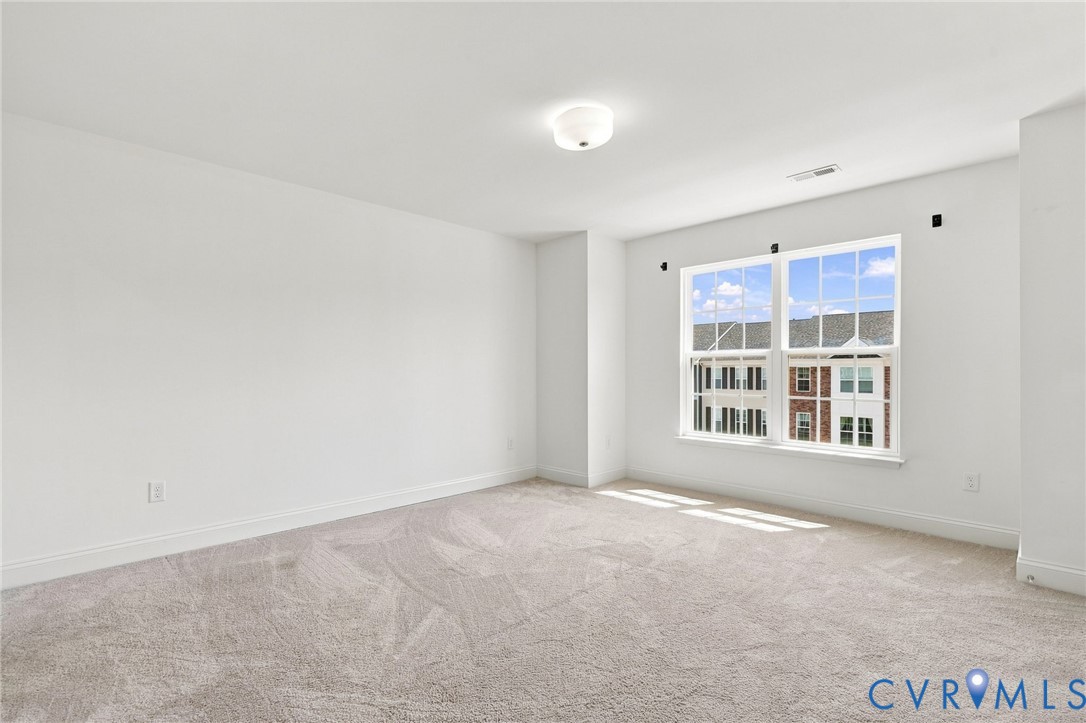Expansive room featuring light-colored carpeting, white wall finishes, a large multi-pane window, and a flush-mount ceiling light fixture