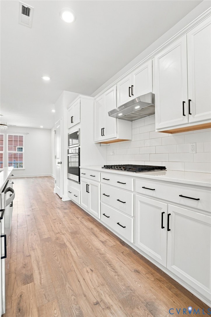 White shaker cabinetry with black hardware, wood-finish flooring, white subway tile backsplash, and stainless steel appliances