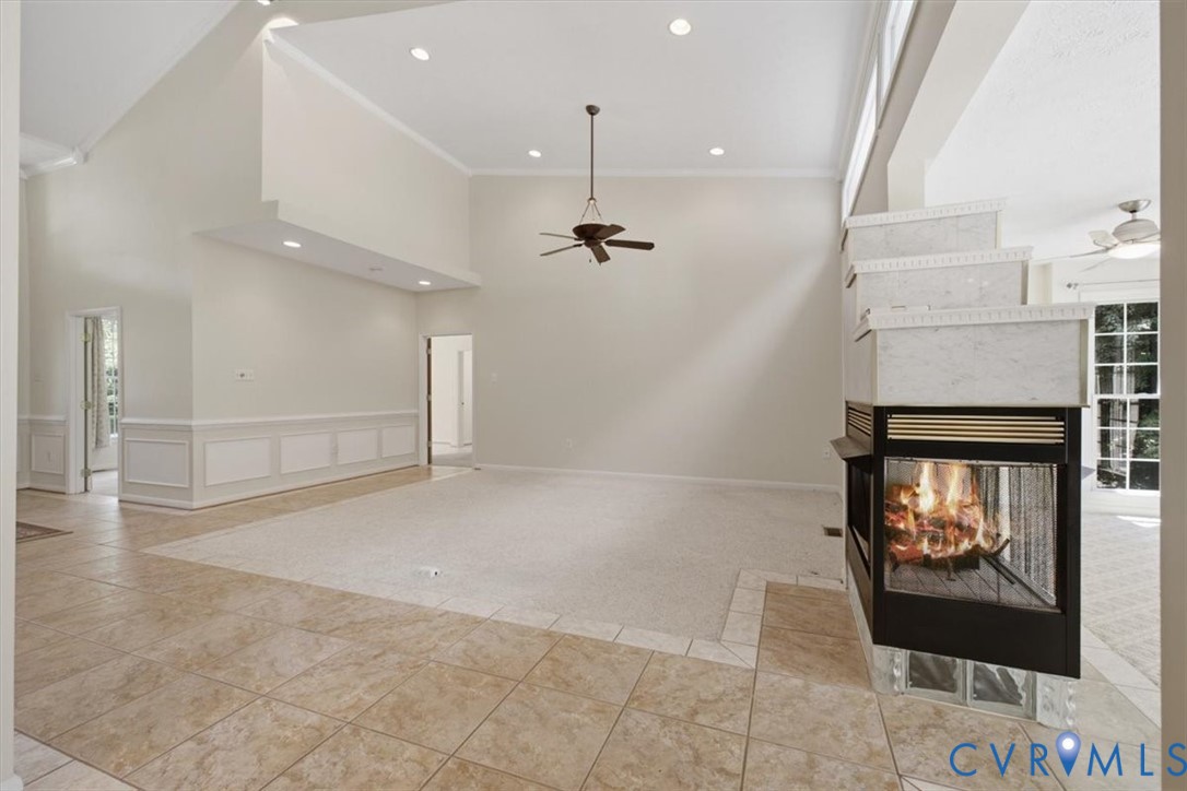 Spacious living area featuring a two-sided fireplace with a tiered surround, high vaulted ceilings, recessed lighting, and a ceiling fan