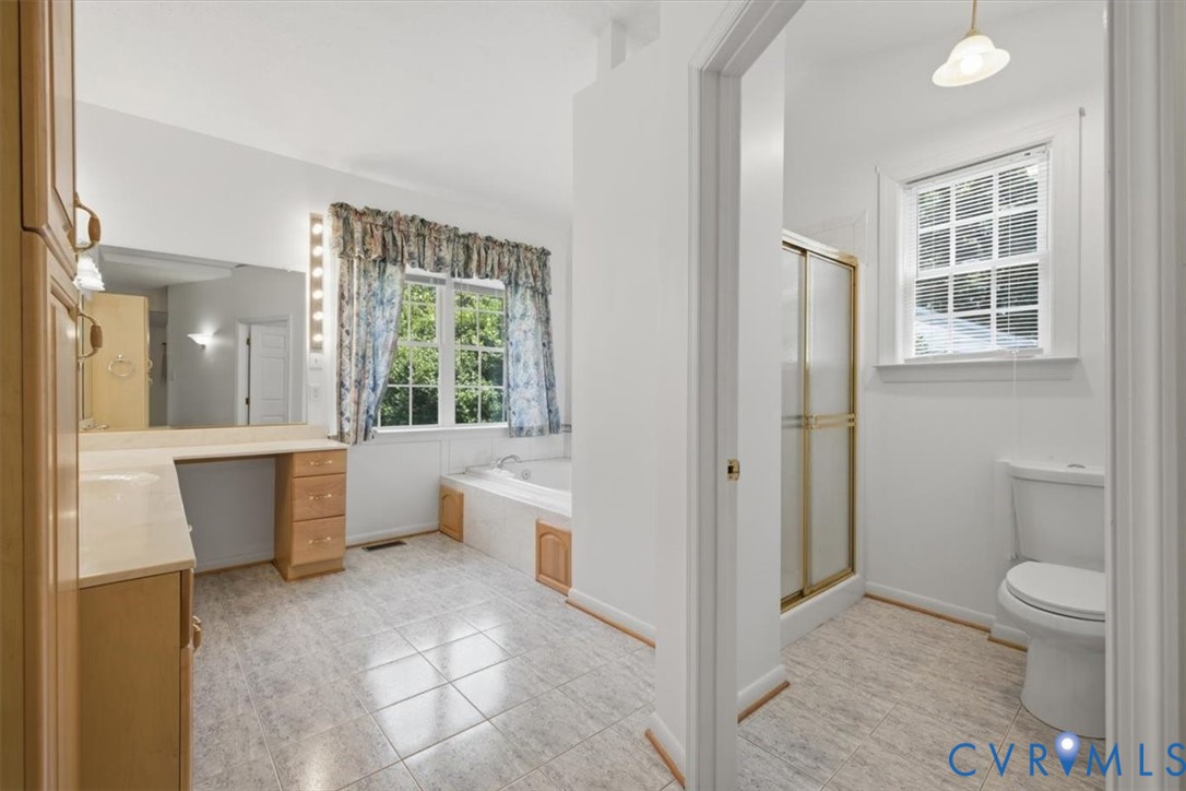 Primary bathroom suite featuring a soaking tub with wood-finish cabinetry, dual vanity with ample counter space, ceramic tile flooring, a separate walk-in shower with brushed brass framing, and a toilet compartment