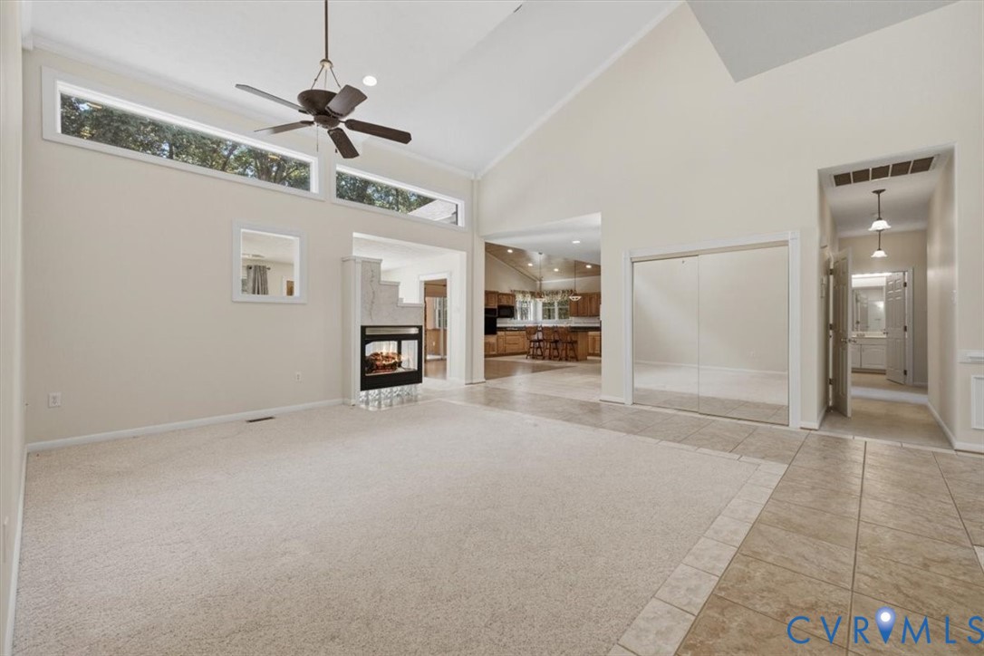Spacious great room with soaring vaulted ceilings, ceiling fan, and abundant natural light from transom windows
