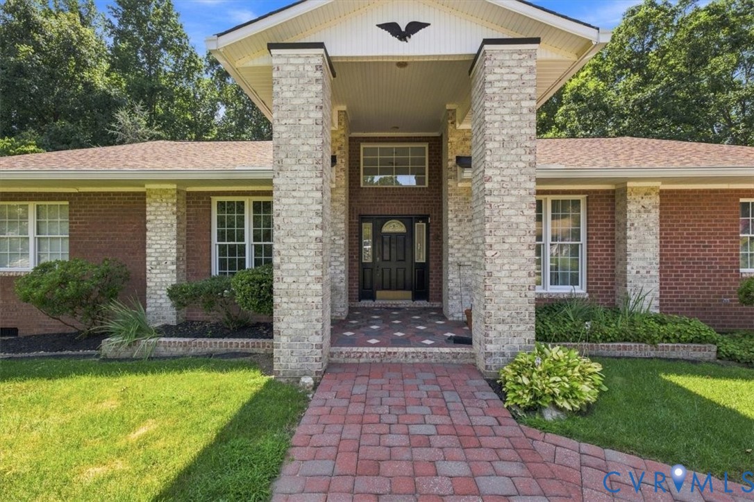 Welcoming brick and stone facade featuring a centered entrance with dark wood doors, flanked by substantial stone columns and topped with a peaked portico Welcoming brick and stone facade featuring a centered entrance with dark wood doors, flanked by substantial stone columns and topped with a peaked portico