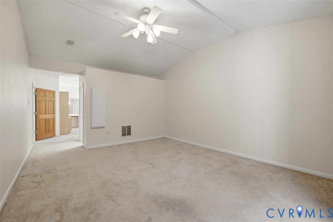 Spacious bedroom with neutral carpet flooring, ceiling fan with integrated lighting, and abundant natural light from multiple windows