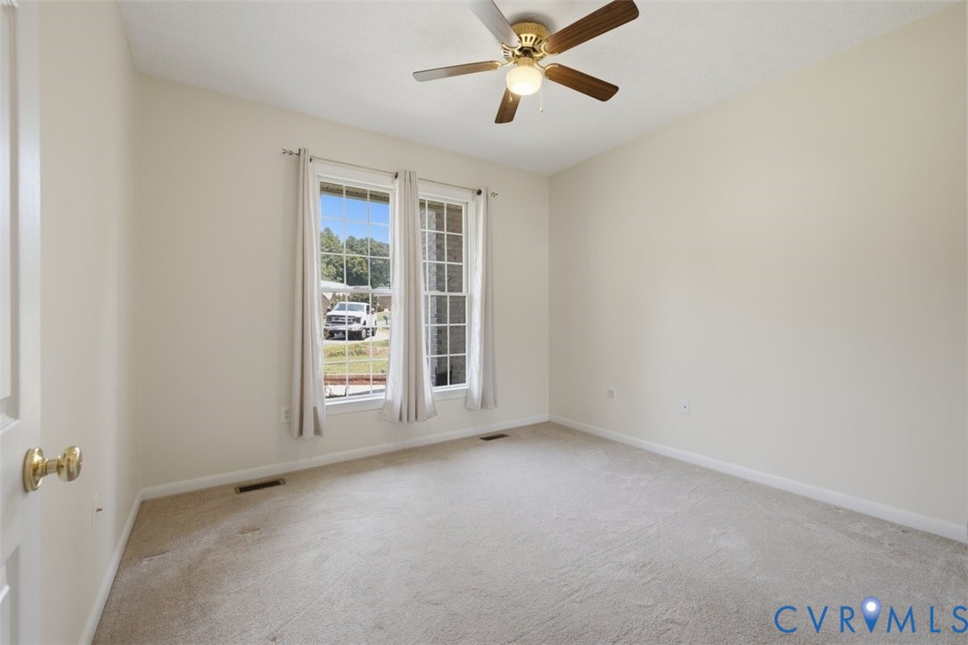 Bright, carpeted bedroom featuring glass French doors with transom windows, ceiling fan with brass fixture, and natural light from dual glass panels overlooking the exterior grounds