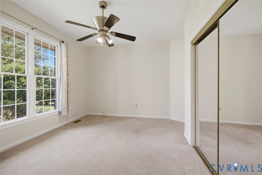 Spacious bedroom flooded with natural light through expansive multi-pane windows, neutral carpet flooring, ceiling fan with integrated lighting, and mirrored sliding-door closet system providing ample storage