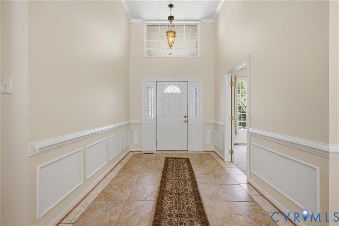 entryway with ceramic tile flooring, decorative wainscoting, and crown molding
