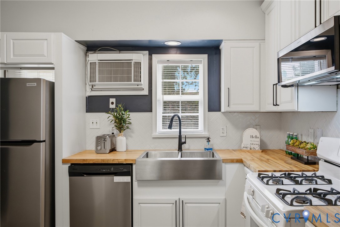 Kitchen featuring white cabinetry, butcher block countertops, stainless steel appliances, a farmhouse sink with a gooseneck faucet, and a white tile backsplash