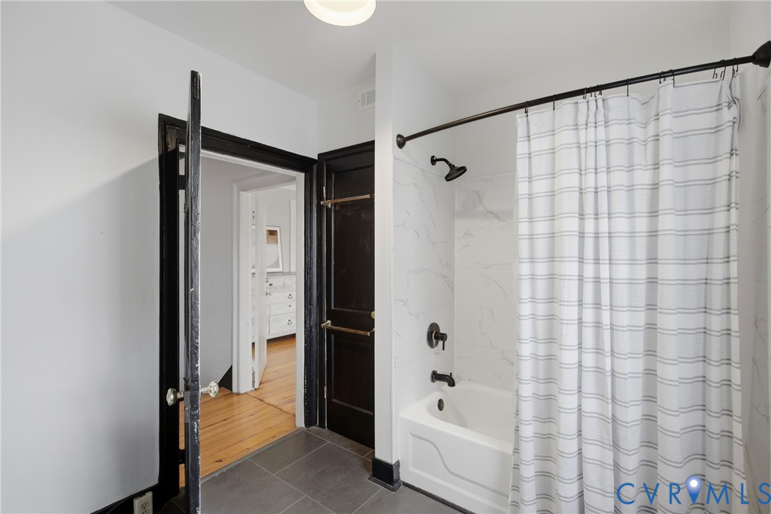 Tub and shower combination with dark bronze fixtures, white subway tile surround, and gray tile flooring
