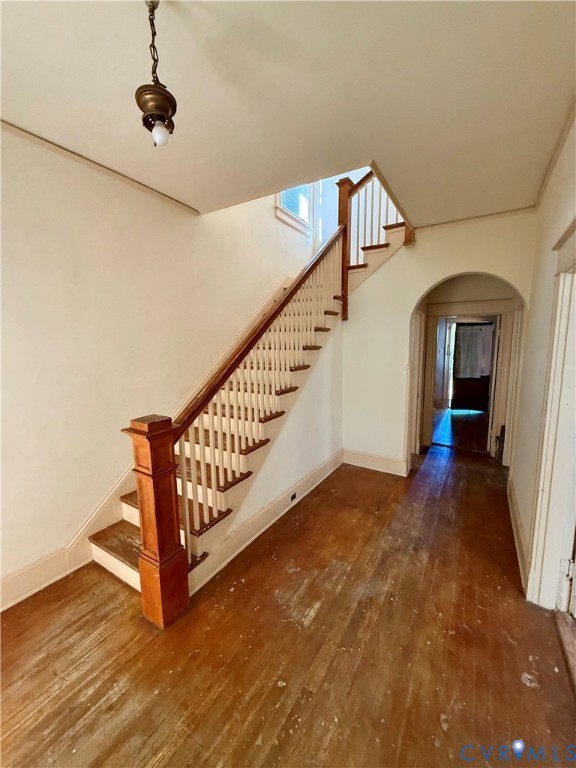 Hardwood flooring, wood staircase with white balusters, wood newel post, arched doorway, and a ceiling-mounted light fixture