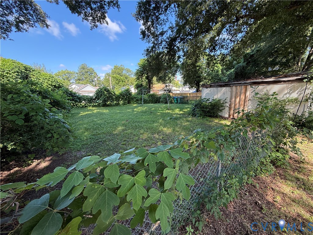 Expansive green lawn, mature perimeter trees, chain-link fencing, and an outbuilding with a corrugated metal roof