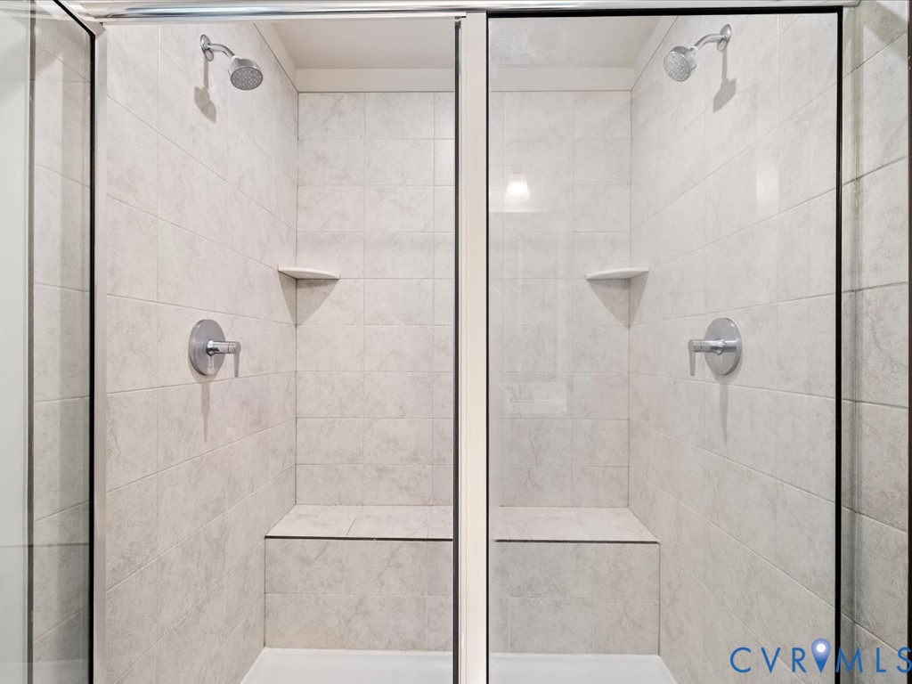 Dual shower stalls featuring full tile surrounds, built-in seating, integrated corner shelving, and glass enclosures