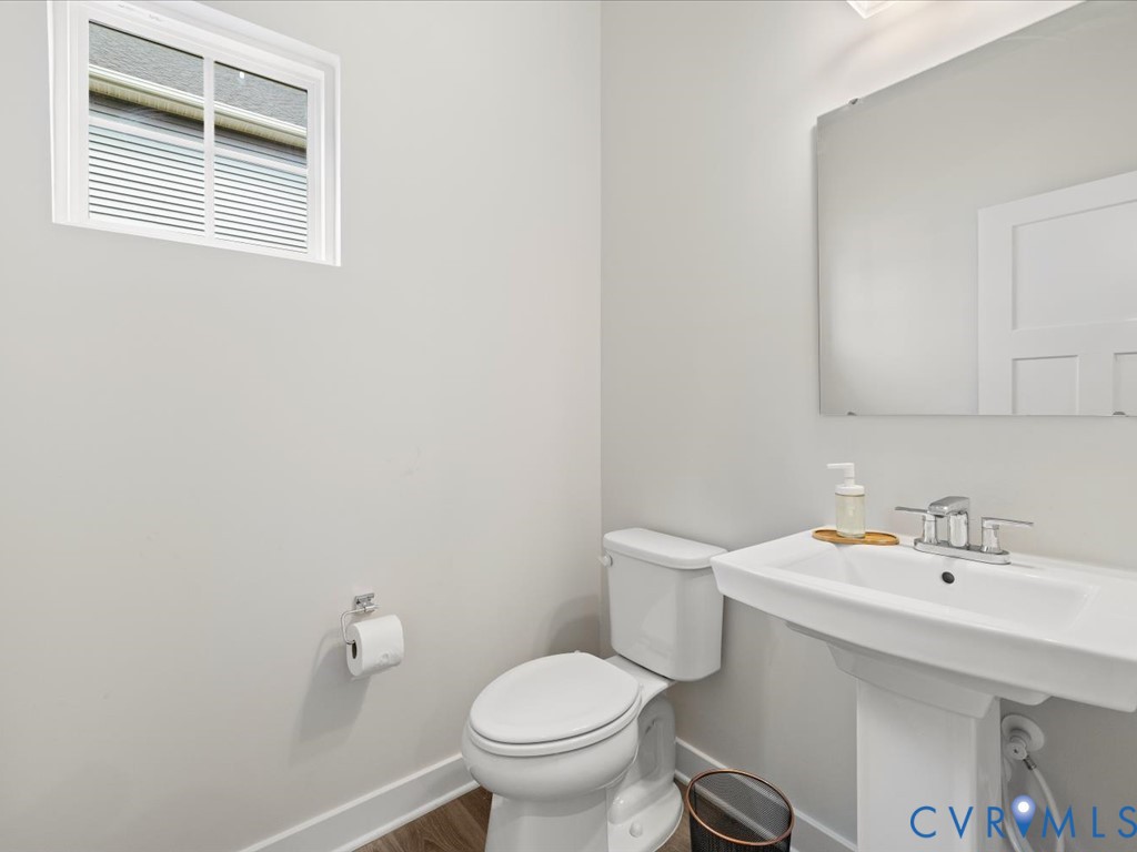 Pedestal sink with chrome faucet, white toilet, and wood-finish flooring