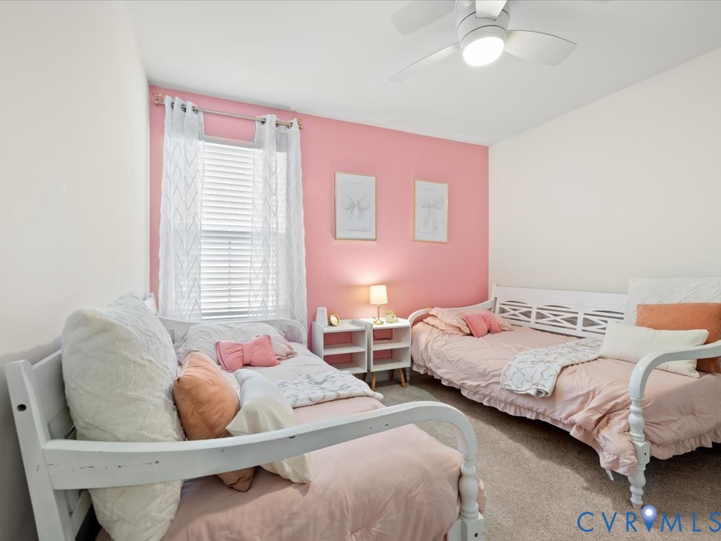 Ceiling fan with integrated lighting, window with blinds and sheer curtains, carpeted flooring, and a vibrant accent wall