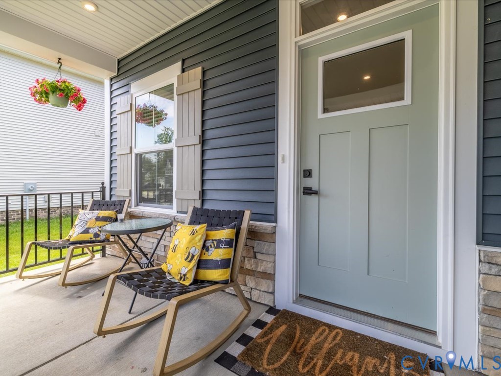 Covered front porch featuring dark blue siding, stone veneer accents, and a light green paneled front door with an upper glass insert