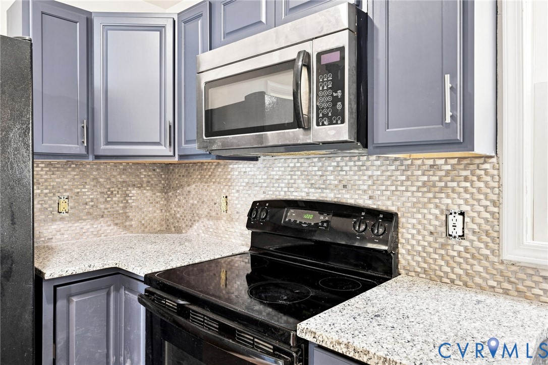 Blue cabinetry with brushed nickel hardware, light speckled countertops, stainless steel microwave, and mosaic tile backsplash