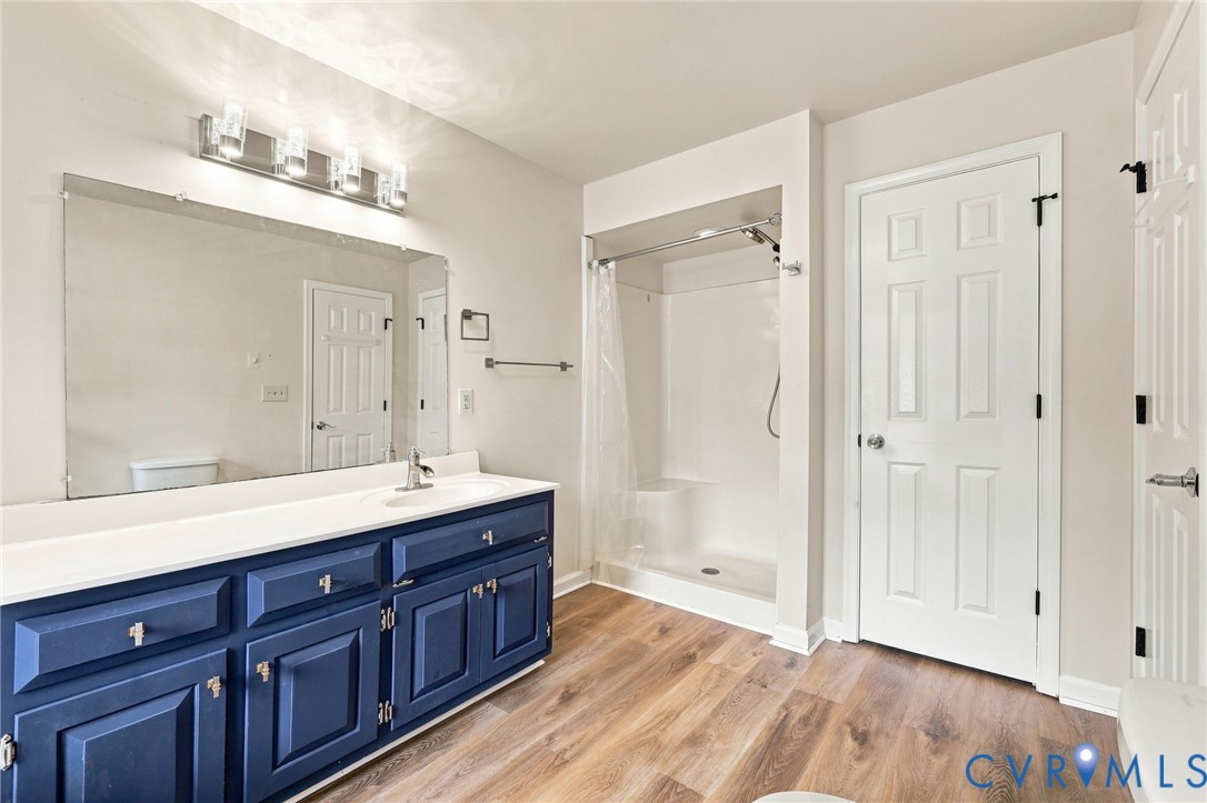 Double vanity with navy cabinetry and white countertop, wood-finish flooring, and a white shower stall