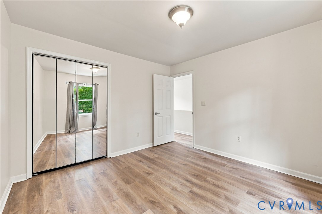 Wood-finish flooring, mirrored closet doors, flush-mount ceiling light, white painted walls, and white trim