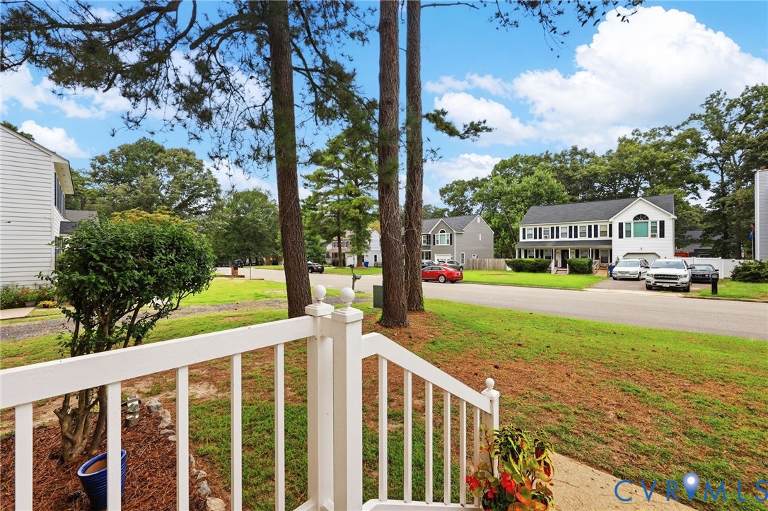 Manicured front yard with mature trees, established landscaping, and white porch railing