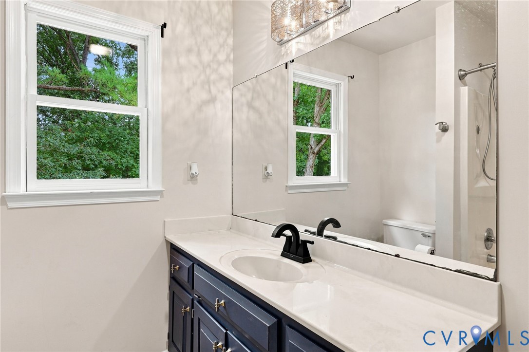 White single-hung window, full-width vanity mirror, dark blue wood-finish vanity, white countertop with integrated sink, and black finish faucet