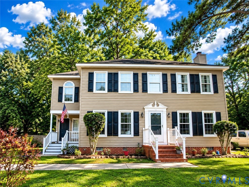 Two-story residence featuring light-colored siding, dark shutters, and a prominent front entrance with a white door and railing Two-story residence featuring light-colored siding, dark shutters, and a prominent front entrance with a white door and railing
