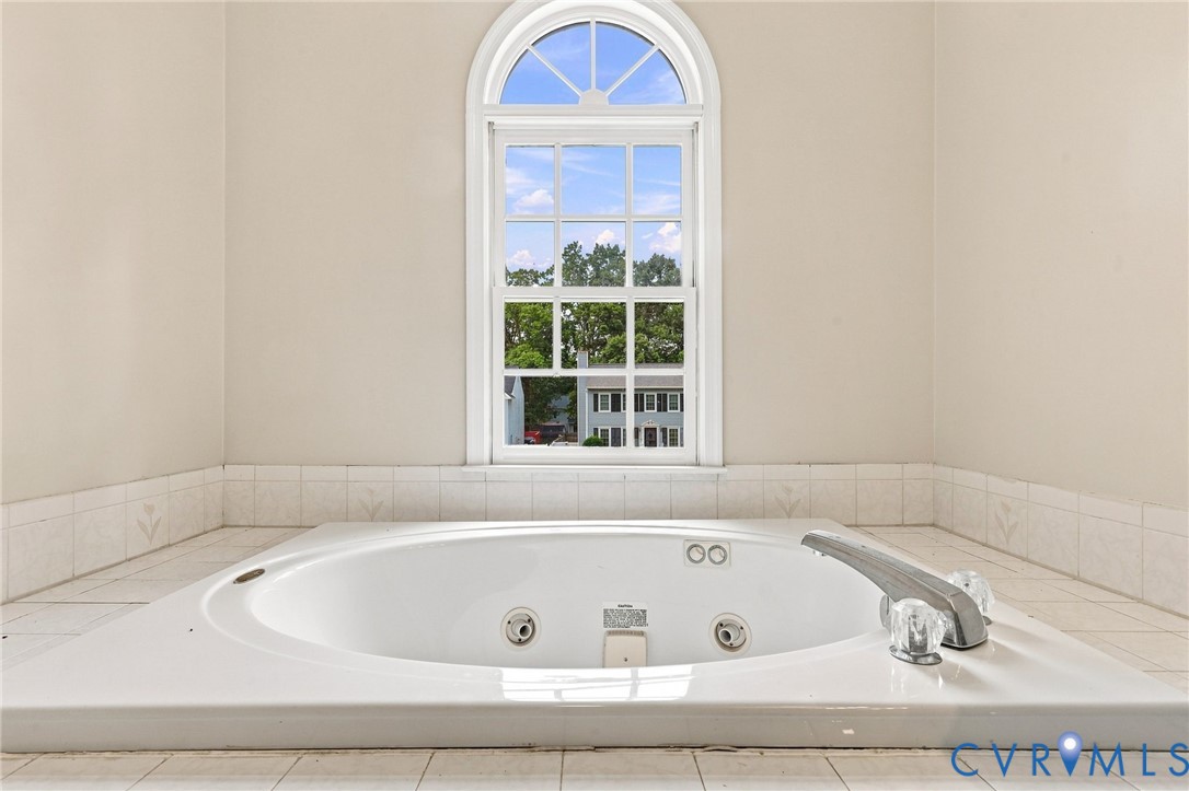 Built-in soaking tub with a tiled surround, arched window, and clear faucet handles