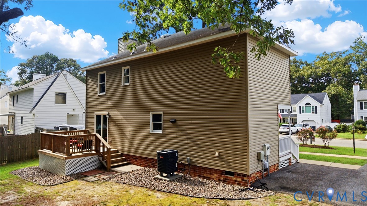 Two-story exterior with light brown siding, a ground-level wood deck with stairs, a paved driveway, and mature landscaping Two-story exterior with light brown siding, a ground-level wood deck with stairs, a paved driveway, and mature landscaping