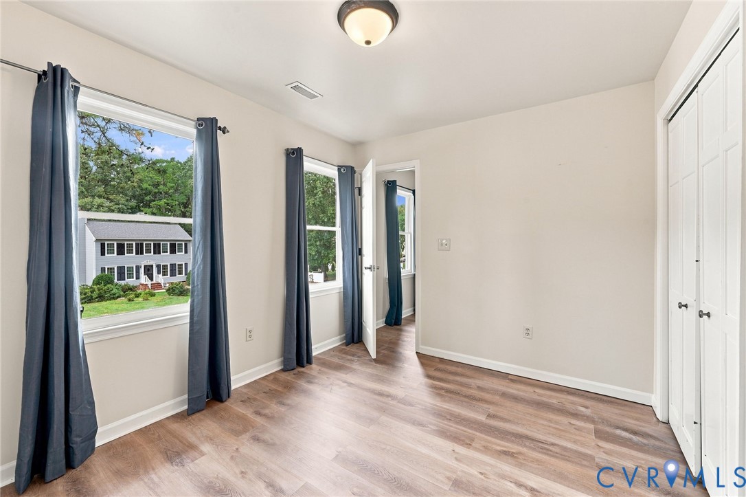 Spacious room featuring wood-finish flooring, multiple windows, a ceiling-mounted light fixture, and a bi-fold closet