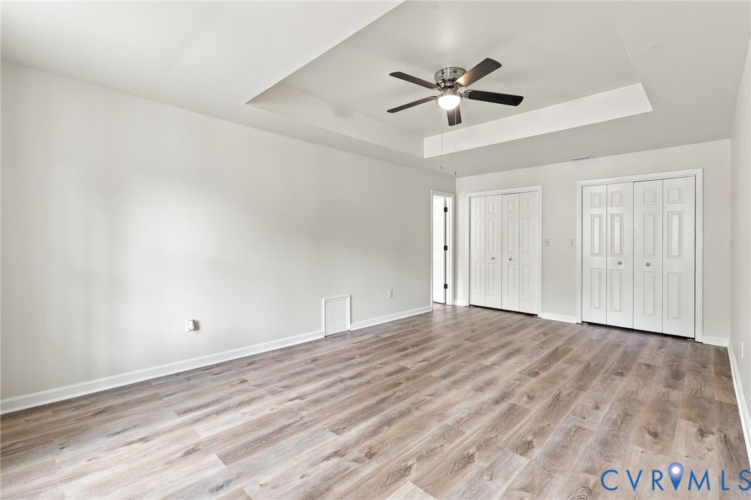 Tray ceiling with a ceiling fan, wood-finish flooring, and white bifold closet doors