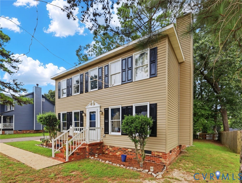 Two-story residence featuring light-colored siding, multiple windows with dark shutters, a front entry with a small porch, and a side chimney