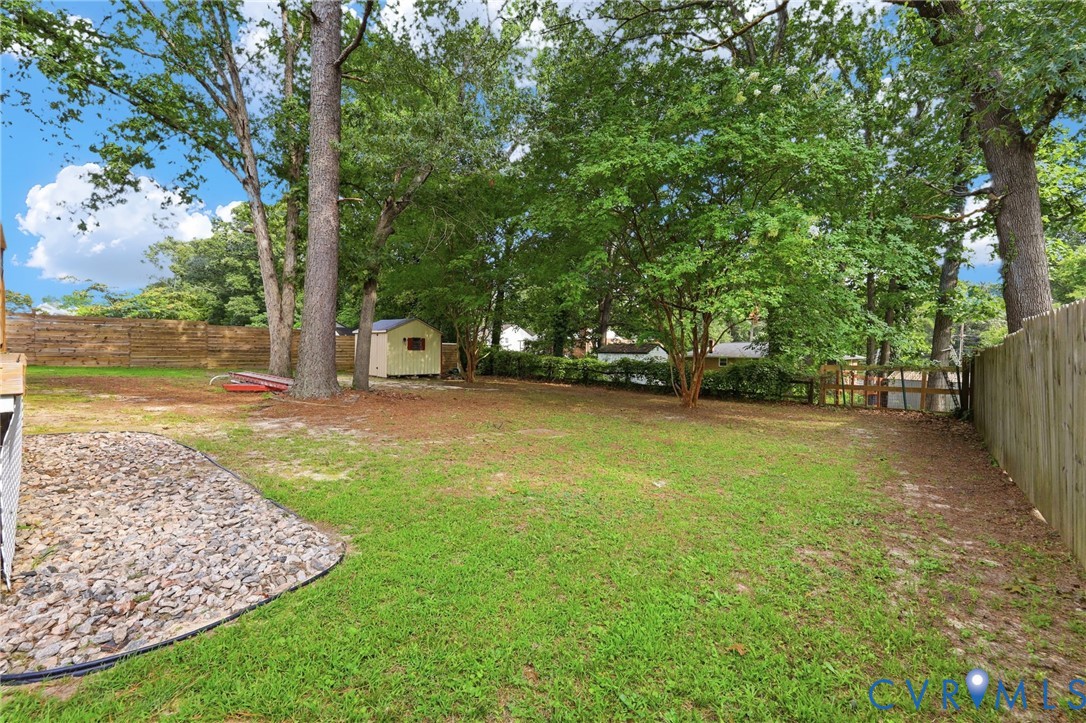Expansive backyard with a manicured lawn, mature trees, wood privacy fencing, a gravel landscaping area, and a storage shed
