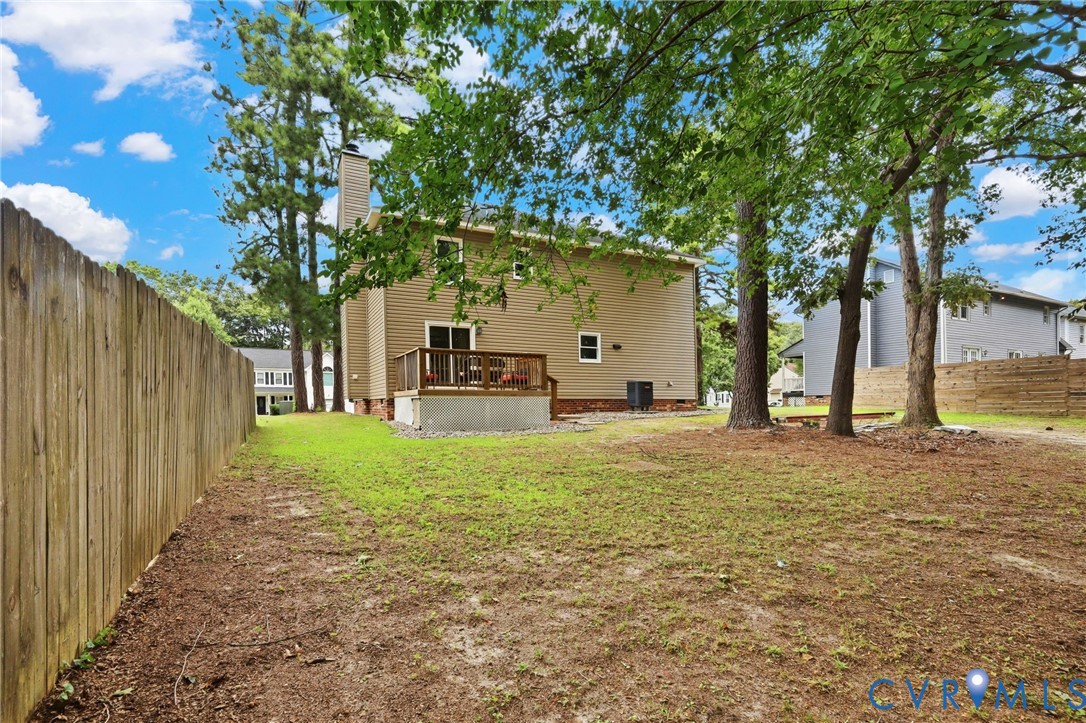 Expansive backyard featuring a wood privacy fence, mature trees, and a raised wood deck with railing