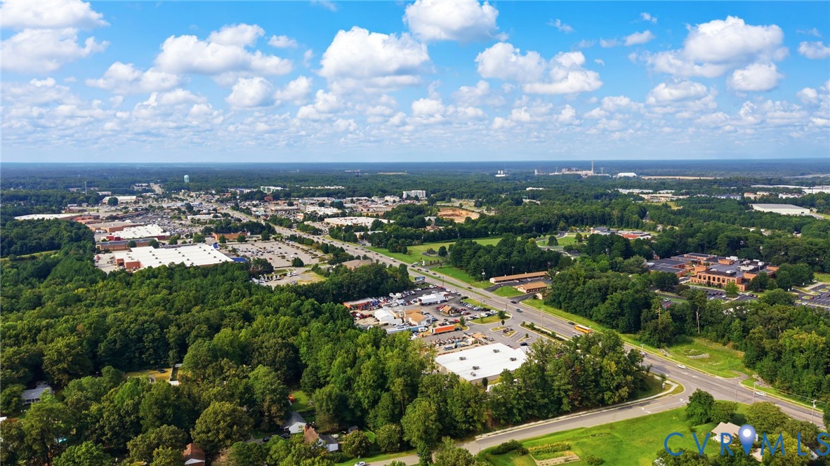Expansive aerial perspective showcasing a developed suburban area with abundant mature trees, multiple commercial structures, and a prominent roadway network