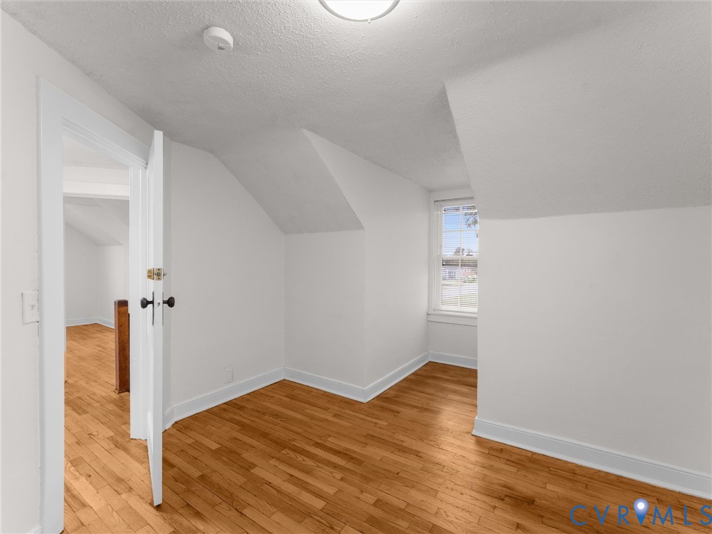 Hardwood flooring extends throughout this room, featuring sloped ceilings and a double-hung window