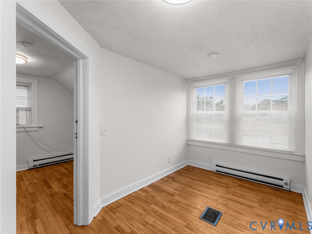 Room featuring wood-finish flooring, white painted walls, and twin windows with blinds