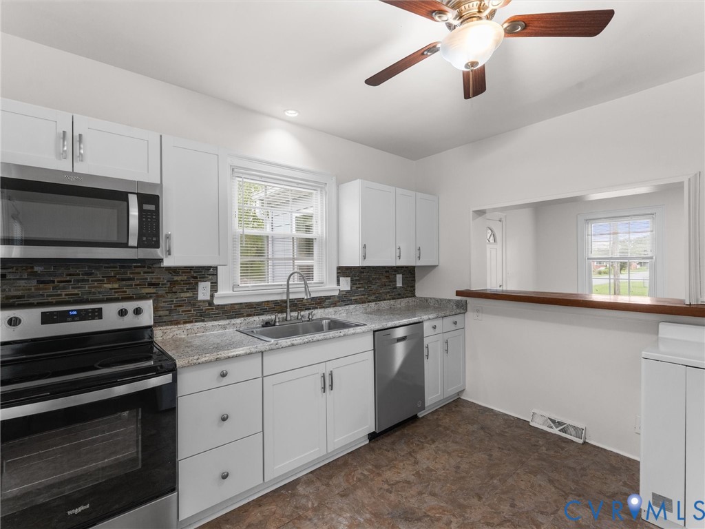 Kitchen featuring white cabinetry, stainless steel appliances, granite-style countertops, mosaic tile backsplash, and a pass-through window with a wood-finish bar top