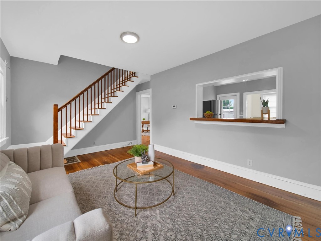 Living area featuring wood-finish flooring, a contemporary ceiling light fixture, a built-in pass-through with a wood-finish shelf, and a staircase with wood-finish handrails and balusters