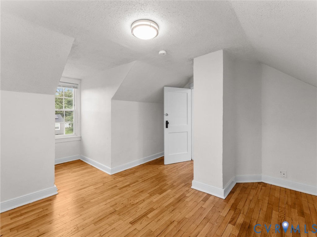 Room featuring sloped ceilings, wood-finish flooring, a double-hung window, and a flush-mount ceiling light