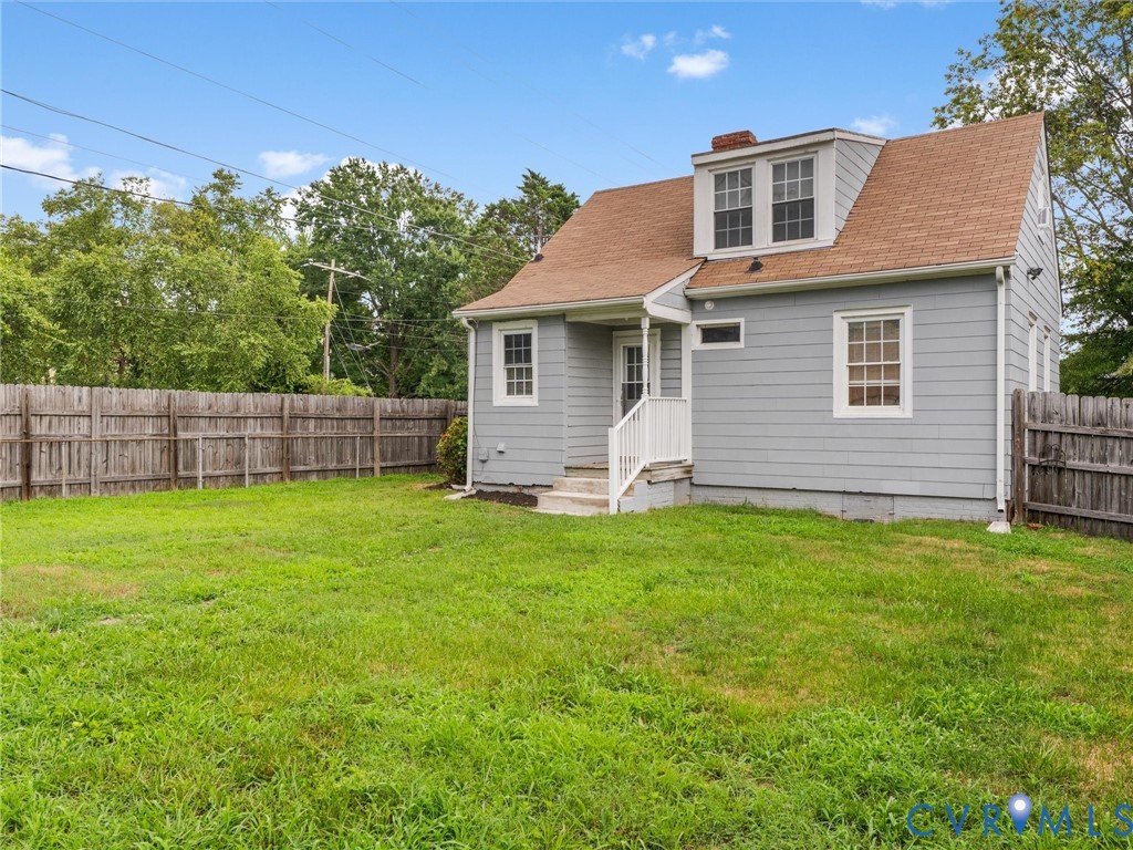 Spacious rear yard with a wooden privacy fence, dormer windows, and a shingled roof