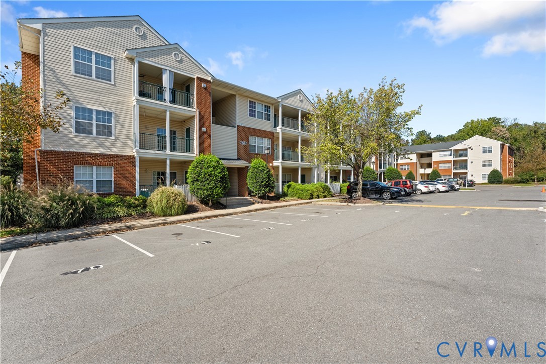 Exterior facade featuring brick masonry, horizontal siding, private balconies, and asphalt-paved parking