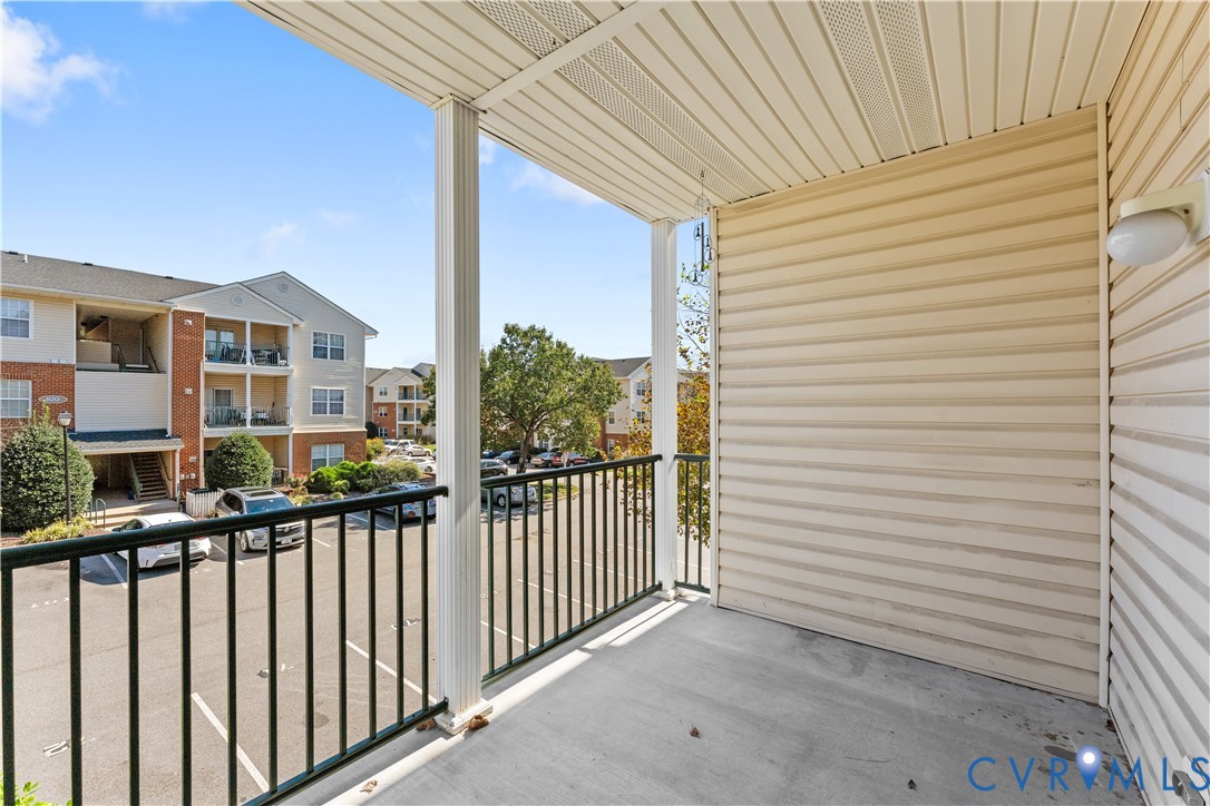 Covered balcony featuring concrete flooring, vinyl siding, and black metal railings