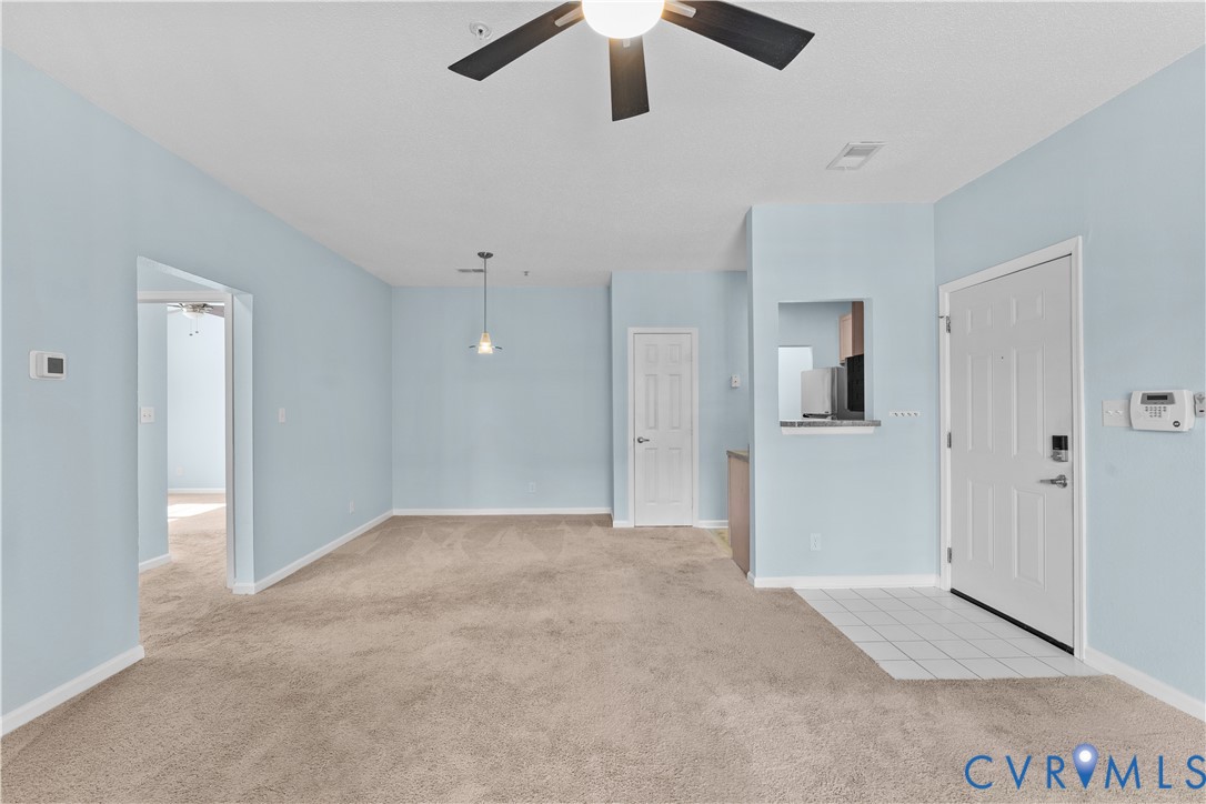 Open interior space featuring a ceiling fan, carpeted flooring, tile entryway, pendant lighting, and a passthrough window