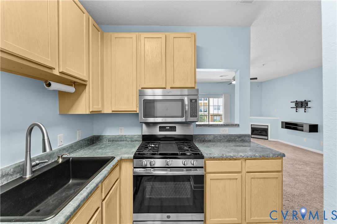 Kitchen featuring light-finish cabinetry, stone-texture laminate countertops, a black undermount sink with a high-arch faucet, and stainless steel gas range with a built-in microwave