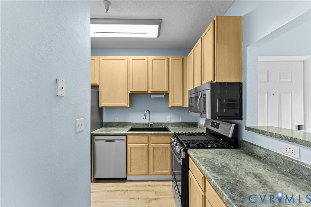 Kitchen featuring light-finish cabinetry, stone-texture countertops, integrated stainless steel appliances, a deep undermount sink with a gooseneck faucet, and wood-finish flooring