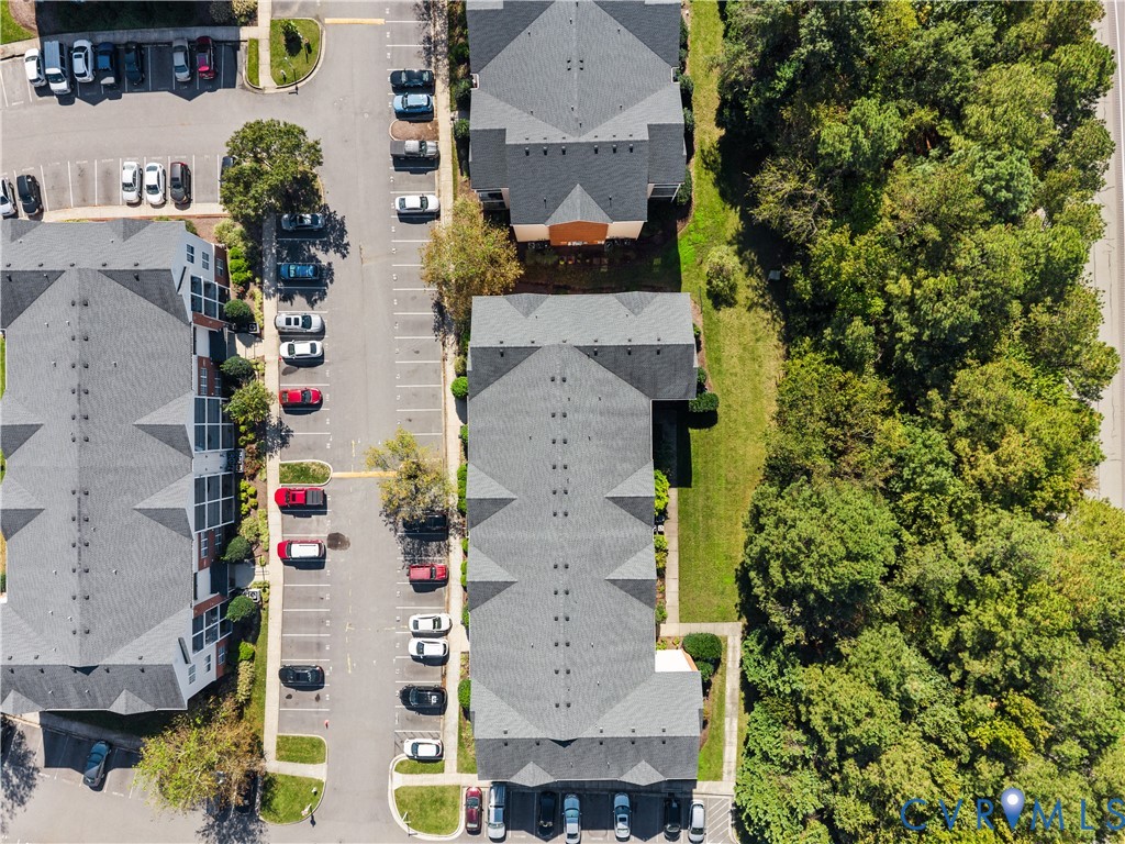 Aerial perspective of multi-building complex featuring asphalt parking surfaces, shingled roofing systems, and dense wooded borders